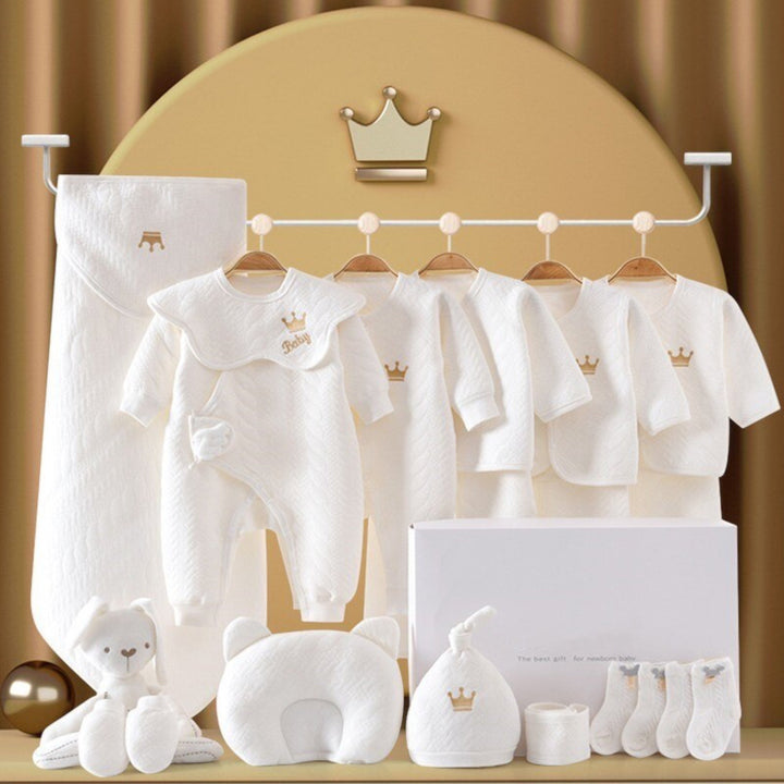 Luxe babypakket flat lay: romper, muts, schoentjes, deken, slabbetje en knuffel voor pasgeborenen.