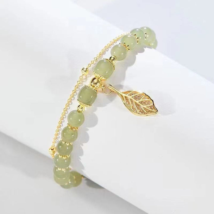 Elegante damesarmband met glanzende jade edelsteen en verfijnde vergulde bladbedel. Verstelbaar sieraad.