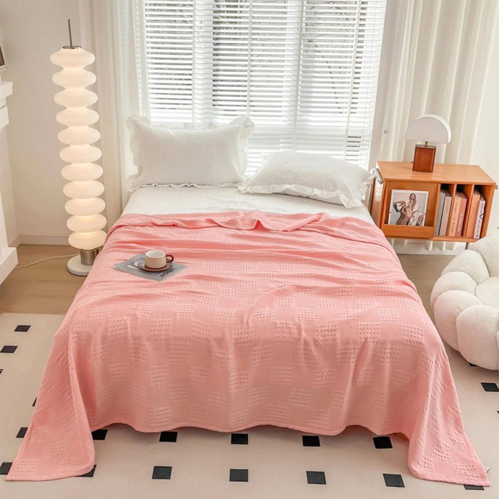 Stijlvolle wafeldeken van biologisch katoen nonchalant gedrapeerd over een slaapkamerbed, voor extra comfort.