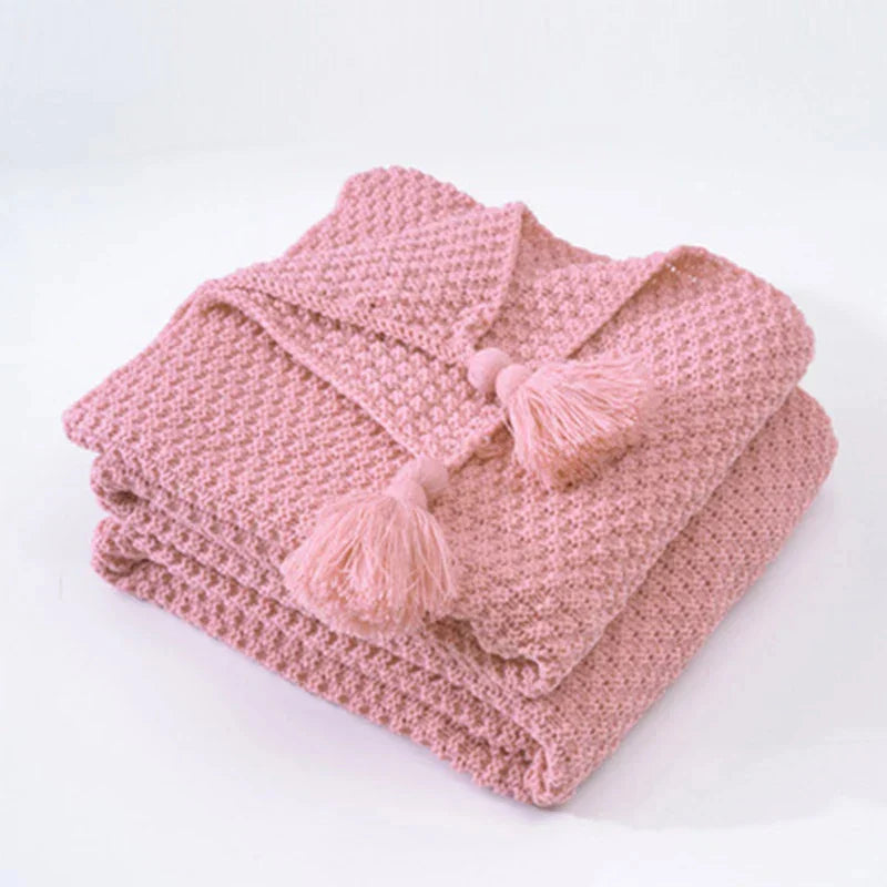 Huiselijk gebreid wollen woonaccessoire; een comfortabele plaid met kwastjes voor je interieur.