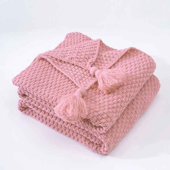 Huiselijk gebreid wollen woonaccessoire; een comfortabele plaid met kwastjes voor je interieur.