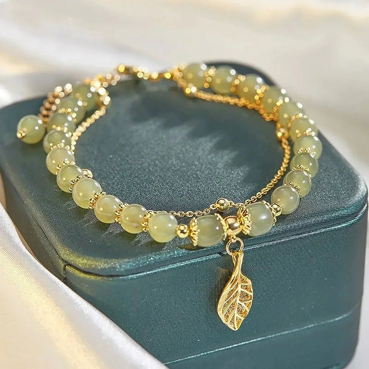 Damesarmband met natuurlijke jade edelsteen kralen en een gedetailleerde vergulde bladbedel. Elegant en verstelbaar.