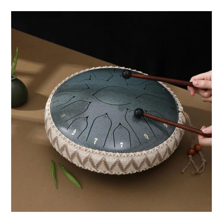 Zilverkleurige stalen tongtrommel met drumstokken en muziekboek op houten tafel. Voor meditatie & rust.