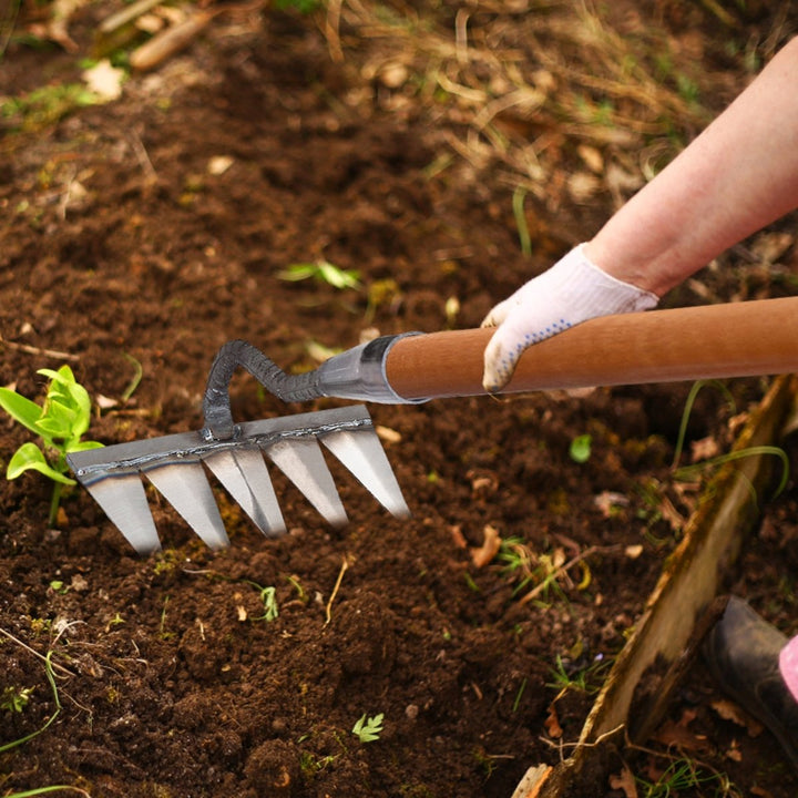 Handen gebruiken de onkruidhark om moeiteloos onkruid te verwijderen uit een tuinperk.