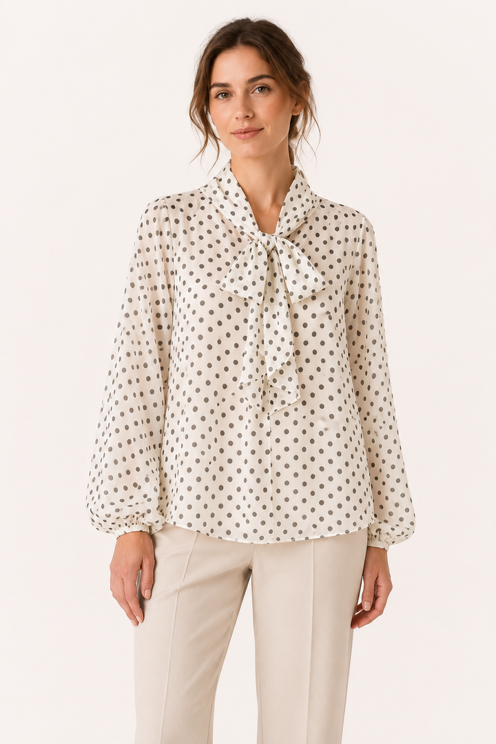 Elegante beige damesblouse met bruine stippenprint, strikdetail en pofmouwen, ideaal voor kantoor of casual chic.
