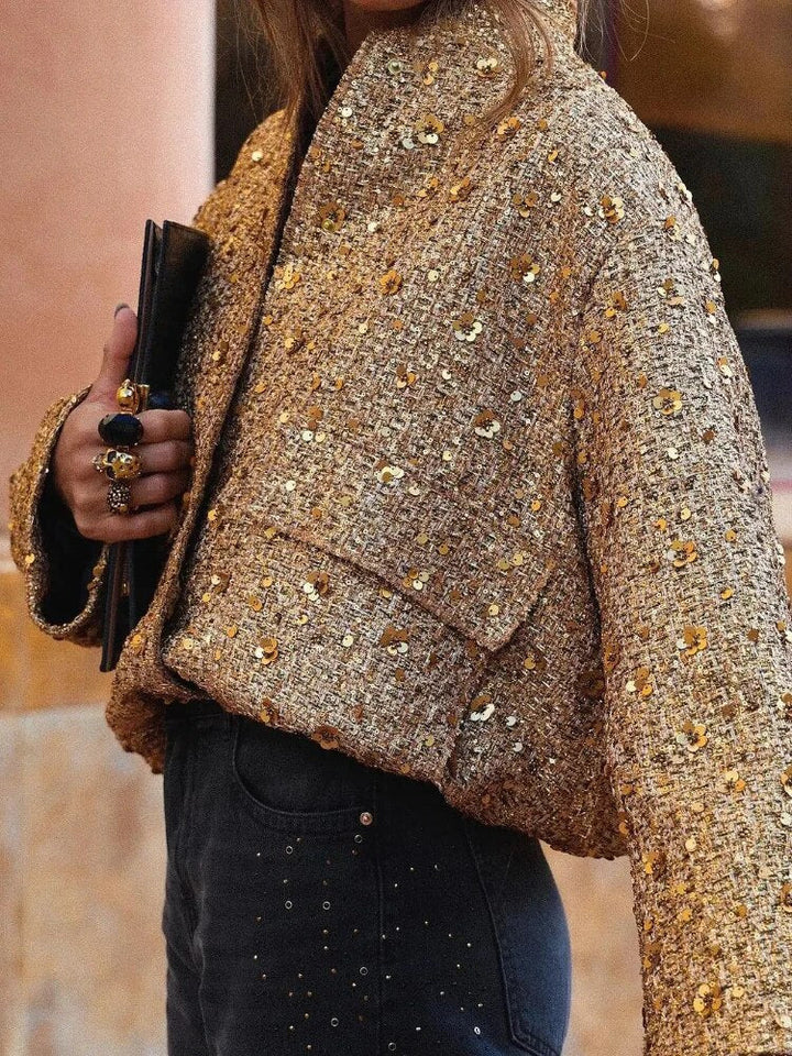 Close-up van de sprankelende stof van de korte dames glitterjas met kraag, toont chique afwerking en comfort.