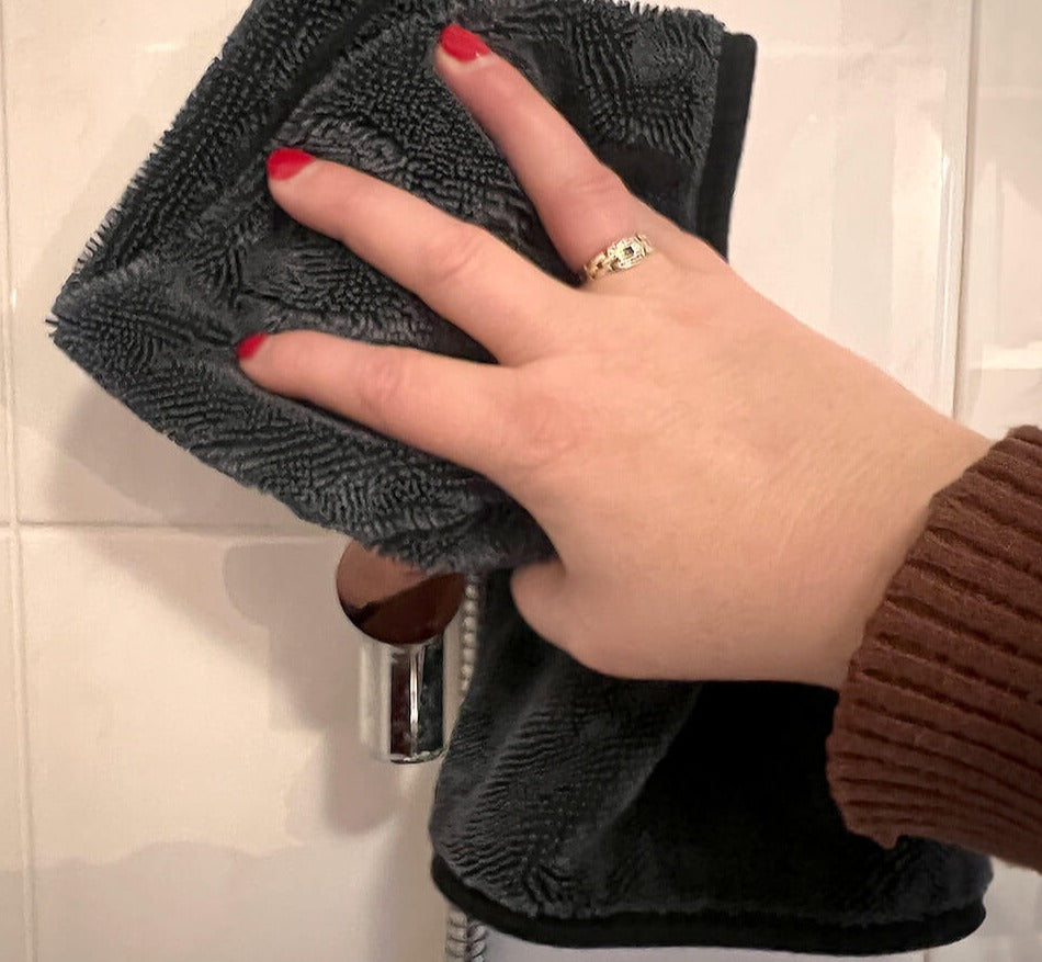 Vrouw poetst spiegel streeploos schoon met de sneldrogende microvezel schoonmaakdoek in de badkamer.