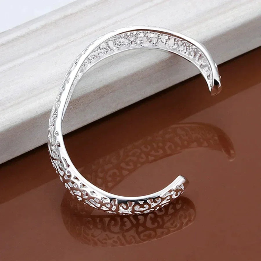 Zilverkleurige filigraan damesarmband elegant gepresenteerd, glanzend en verfijnd sieraad.
