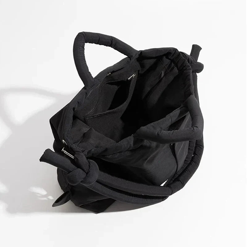 Vrouw draagt trendy zwarte puffer handtas als schoudertas. Perfect voor een moderne look, een must-have accessoire.
