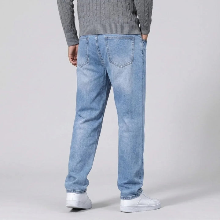 Zittende man toont de flexibele, comfortabele pasvorm van de lichtblauwe straight leg herenjeans.