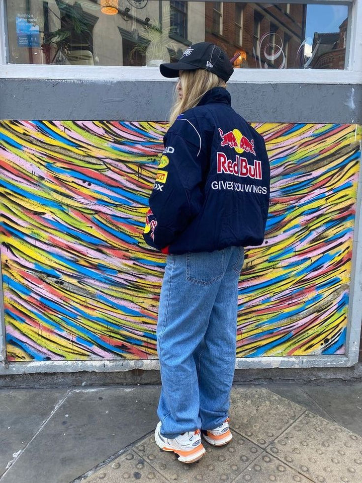 Moderne donkerblauwe racingjas, unisex, met hoge kraag en volledige ritssluiting, streetwear look.