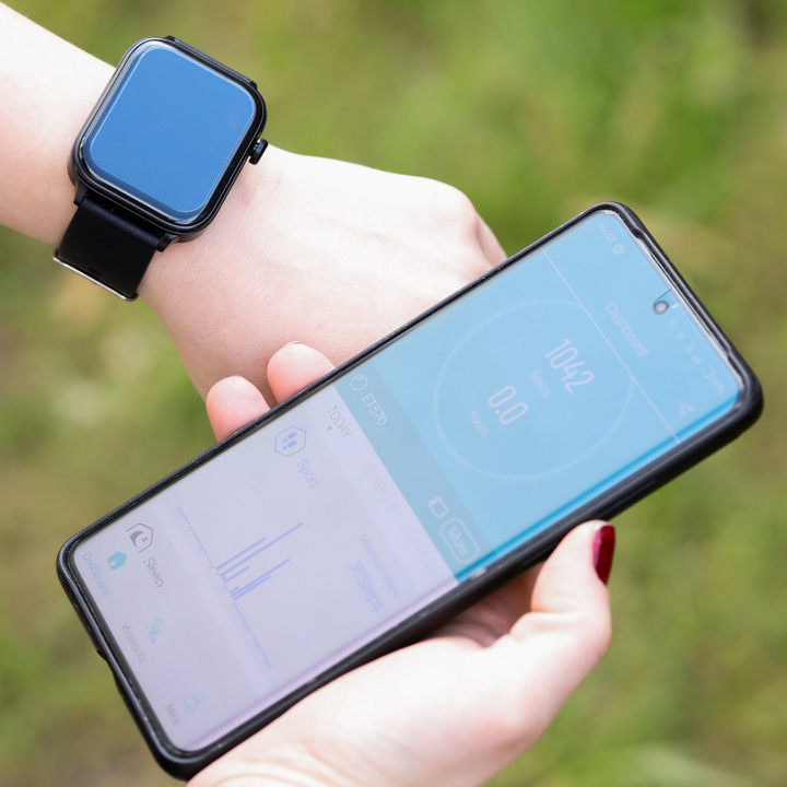 Zwarte wearable smartwatch naast een smartphone (iOS/Android). Geeft meldingen en gezondheidsinzichten weer.