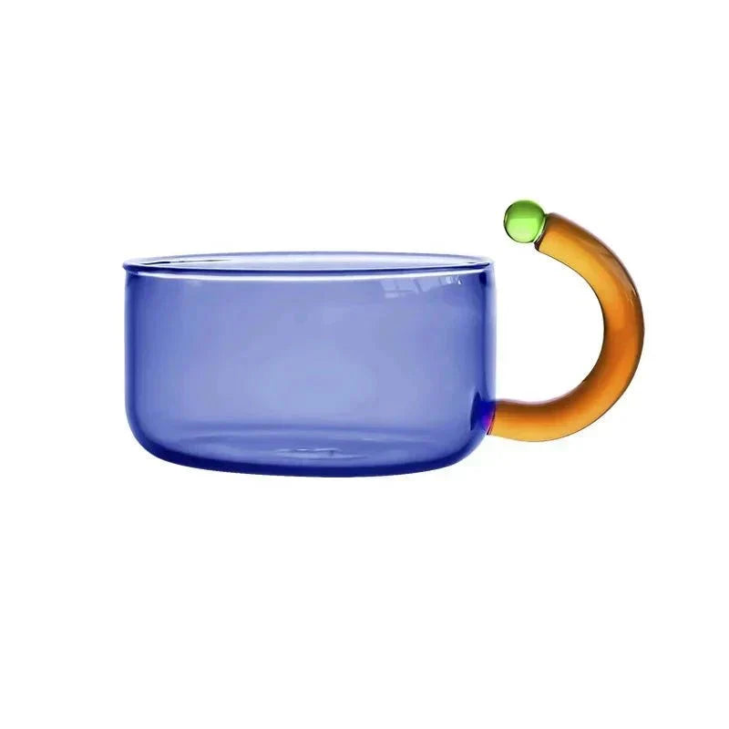 Glazen waterketel met grijze accenten en een blauwe mok, onderdeel van de complete theeset.