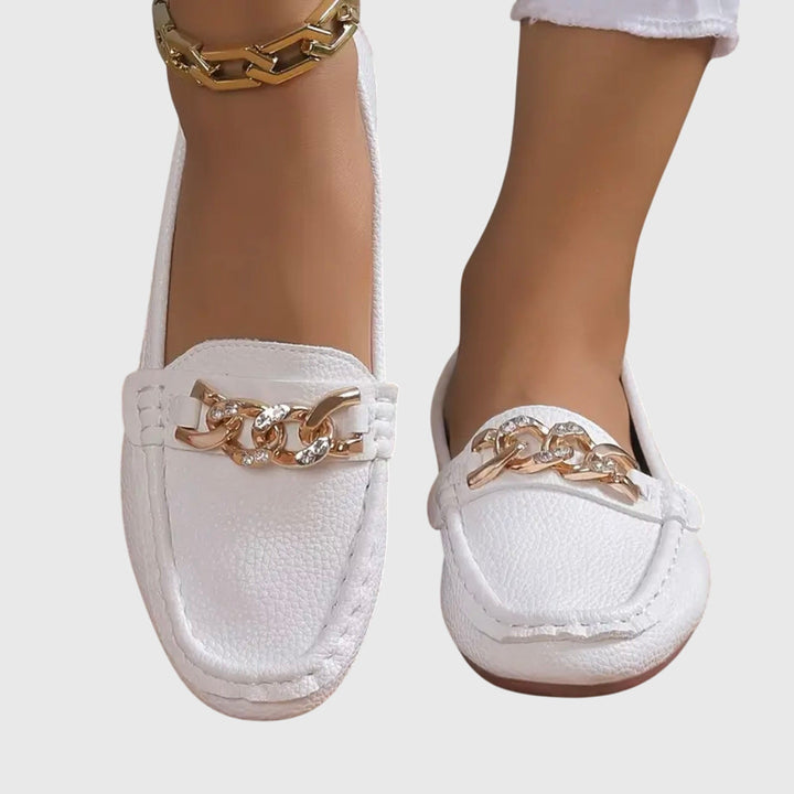 Zijaanzicht van dames loafers met gouden ketting, platte zool en elegant design. Perfecte instapschoenen.