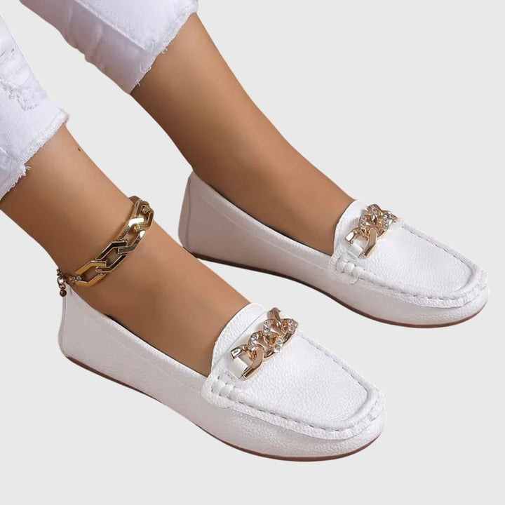 Close-up van gouden kettingdetail op beige dames loafers met comfortabele platte zool. Elegante schoenen.