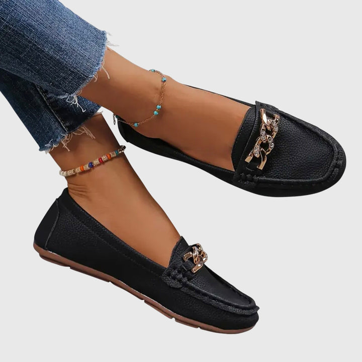 Zwarte dames loafers met gouden kettingdetail. Comfortabele en elegante instapschoenen met platte zool.