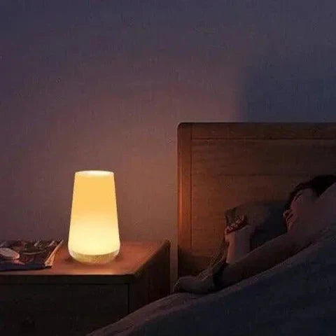 Compacte draagbare LED sfeerlamp met touch control op een nachtkastje, creëert rustige slaapkamer sfeer.
