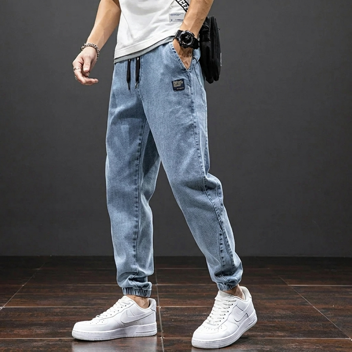 Volledige weergave van de heren denim joggingbroek, een veelzijdige en comfortabele spijkerbroek met jogger-stijl voor heren.