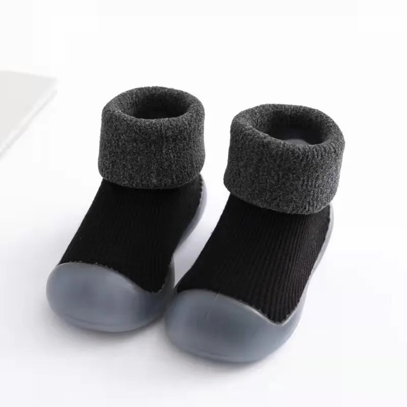 Lachende peuter speelt met comfortabele en warme antislip sokschoenen aan de voetjes.