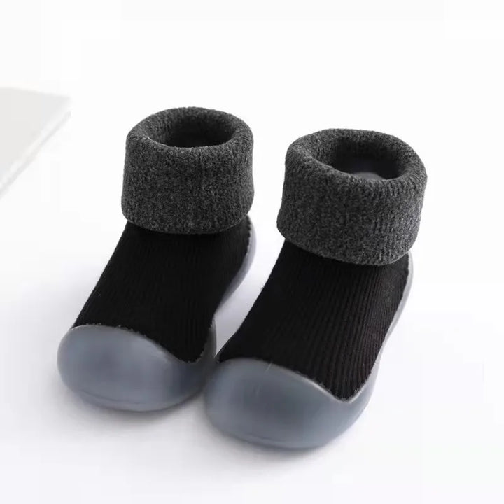 Lachende peuter speelt met comfortabele en warme antislip sokschoenen aan de voetjes.