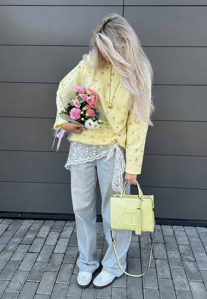 Model draagt gele oversized dames trui met bloemenprint en lange mouwen. Casual en comfortabele dameskleding.