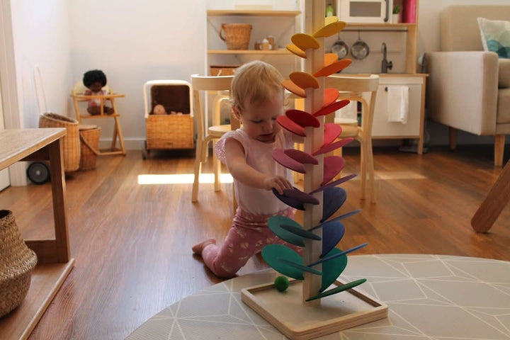 Kind speelt met de houten klankboom, marmerballen rollen langs kleurrijke blaadjes, creëert melodie.