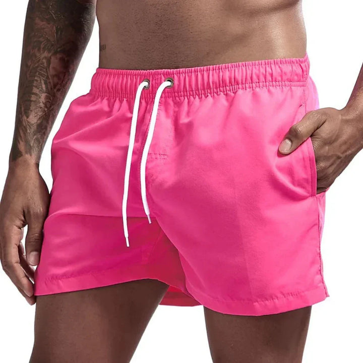 Man draagt stijlvolle, sneldrogende heren zwemshorts op het strand, genietend van de zomerzon.
